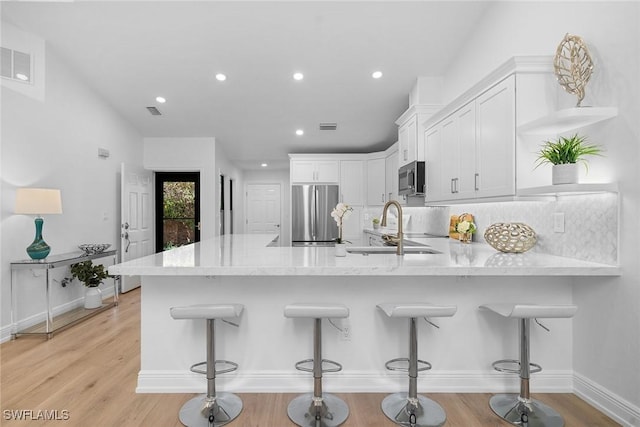 kitchen with a sink, a peninsula, white cabinets, and stainless steel appliances