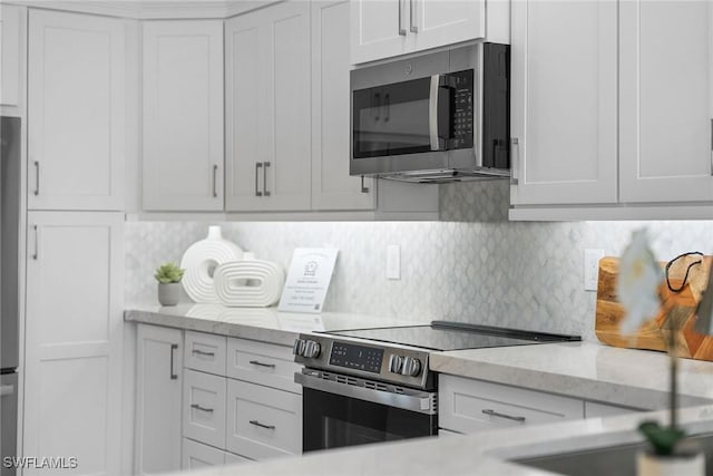 kitchen featuring stainless steel appliances, light stone countertops, tasteful backsplash, and white cabinets