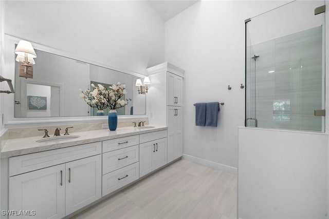 bathroom with double vanity, a shower stall, baseboards, and a sink