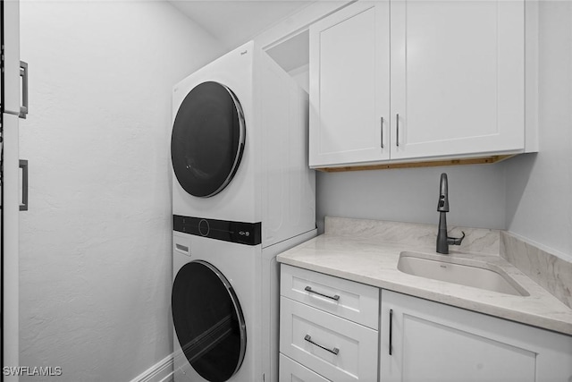 clothes washing area with stacked washer and dryer, cabinet space, a textured wall, and a sink