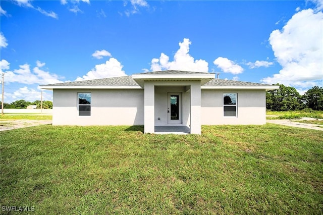 rear view of house featuring stucco siding, a lawn, and a shingled roof