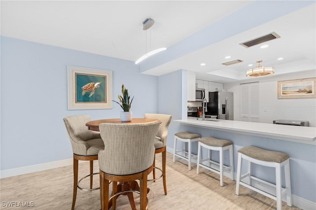 dining space with light wood finished floors, visible vents, baseboards, a tray ceiling, and recessed lighting