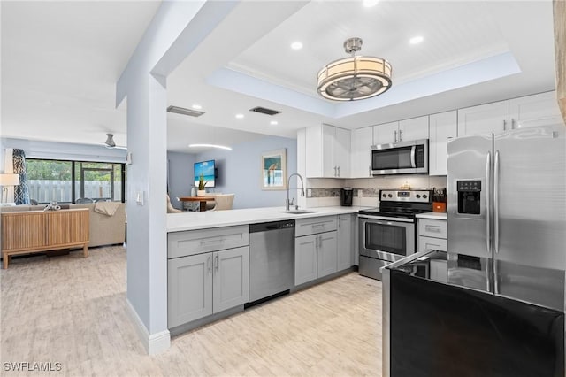 kitchen with light wood-style flooring, gray cabinets, a sink, appliances with stainless steel finishes, and a raised ceiling