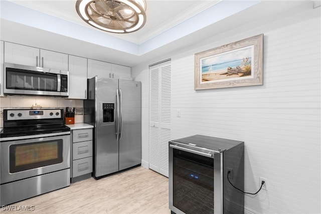 kitchen featuring light wood finished floors, stainless steel appliances, wine cooler, crown molding, and a raised ceiling