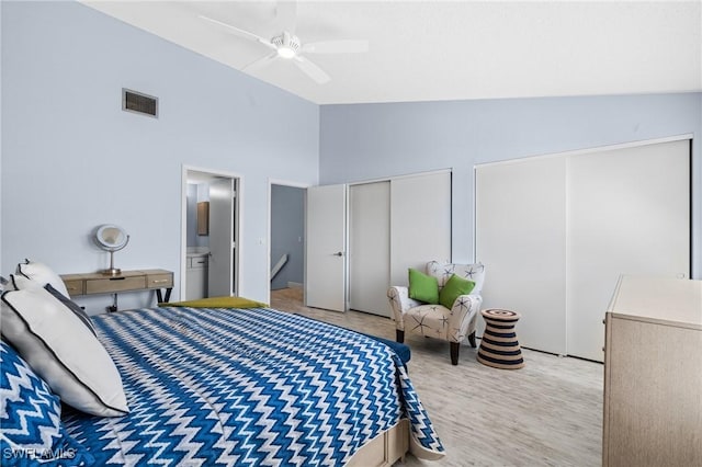 bedroom featuring a ceiling fan, visible vents, vaulted ceiling, light wood-style floors, and two closets