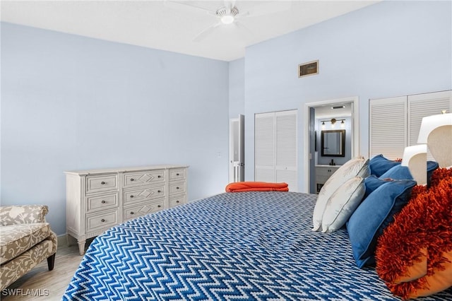 bedroom with visible vents, two closets, light wood-style flooring, a ceiling fan, and a high ceiling