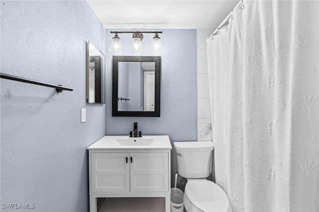 bathroom with vanity, toilet, and a textured wall