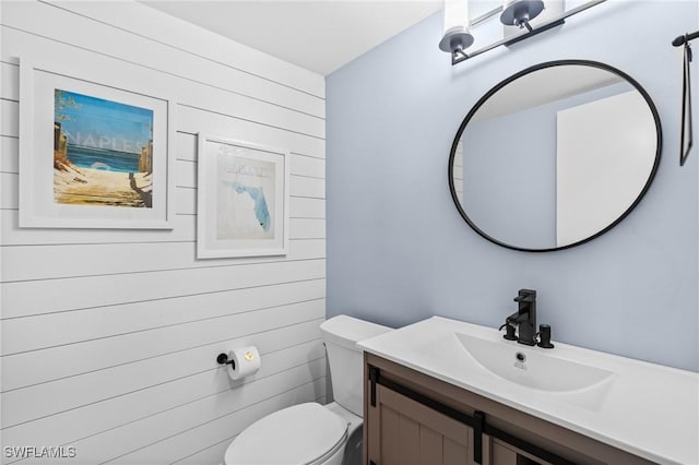 bathroom featuring wood walls, toilet, and vanity