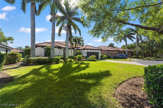 view of front facade with stucco siding, a tile roof, concrete driveway, a front yard, and an attached garage