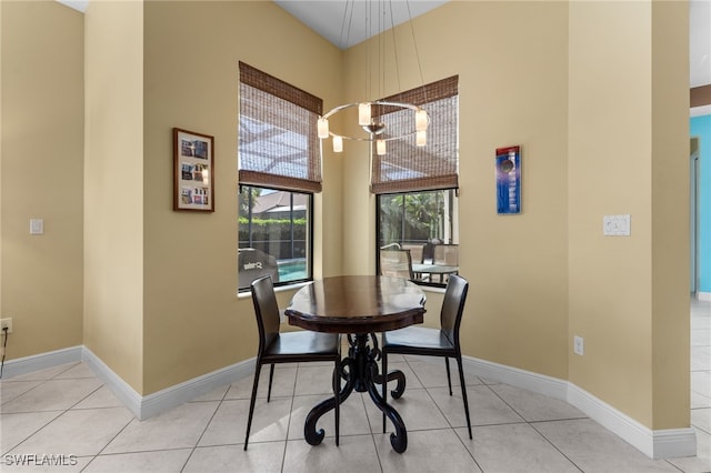 dining space featuring tile patterned flooring, a high ceiling, a notable chandelier, and baseboards