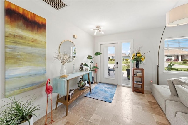 foyer with vaulted ceiling, stone tile floors, baseboards, and visible vents