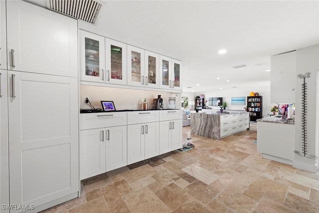 kitchen with stone finish floor, a kitchen island, recessed lighting, white cabinets, and glass insert cabinets