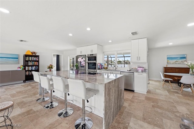 kitchen featuring visible vents, a kitchen island, stone finish floor, stainless steel appliances, and a sink