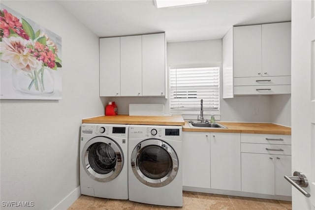 washroom with a sink, baseboards, cabinet space, and independent washer and dryer