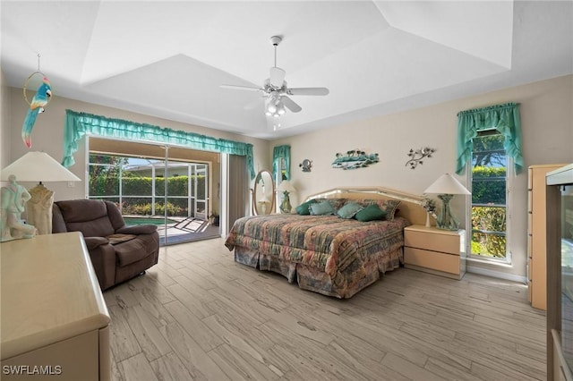 bedroom featuring a ceiling fan, a raised ceiling, wood finished floors, and access to exterior