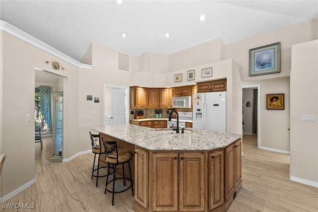 kitchen with a sink, white appliances, light wood-style flooring, and brown cabinetry