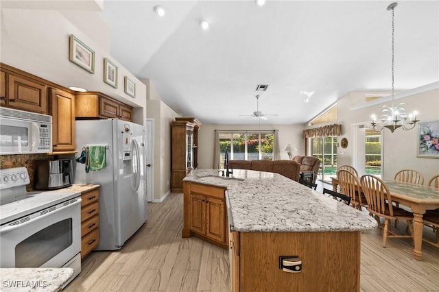 kitchen with white appliances, light stone counters, a sink, vaulted ceiling, and brown cabinets