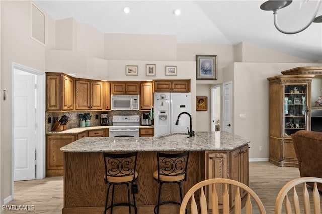 kitchen featuring visible vents, a sink, brown cabinetry, white appliances, and a kitchen island with sink