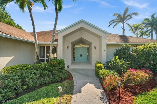 property entrance featuring a shingled roof and stucco siding