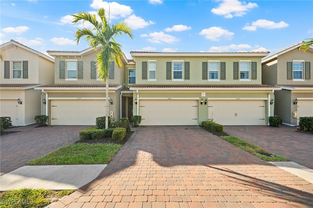 multi unit property with a tiled roof, decorative driveway, a garage, and stucco siding