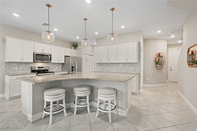 kitchen featuring a breakfast bar, a kitchen island with sink, a sink, appliances with stainless steel finishes, and white cabinetry