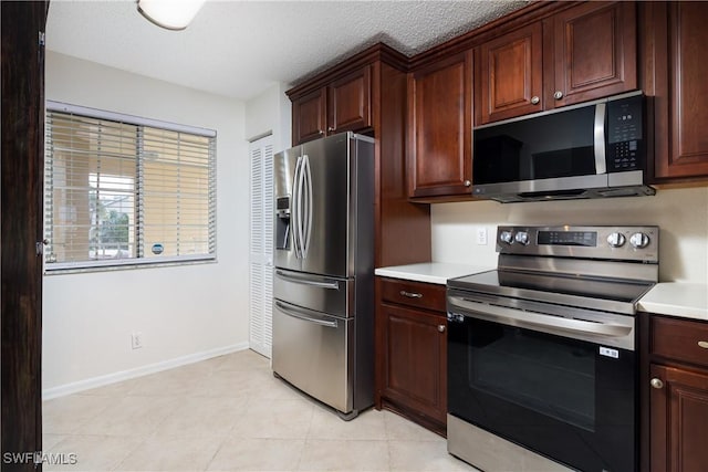 kitchen featuring baseboards, light countertops, appliances with stainless steel finishes, light tile patterned flooring, and a textured ceiling