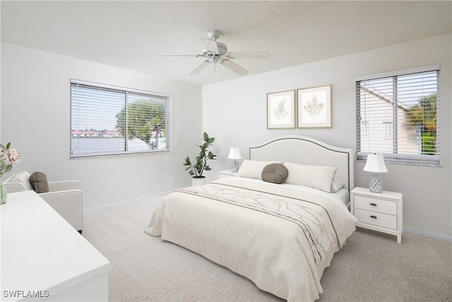 bedroom featuring light carpet, a textured ceiling, baseboards, and a ceiling fan