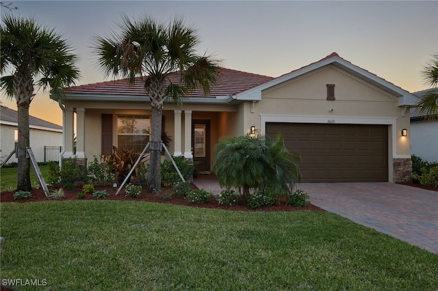 view of front of house featuring a tile roof, a front yard, stucco siding, decorative driveway, and a garage