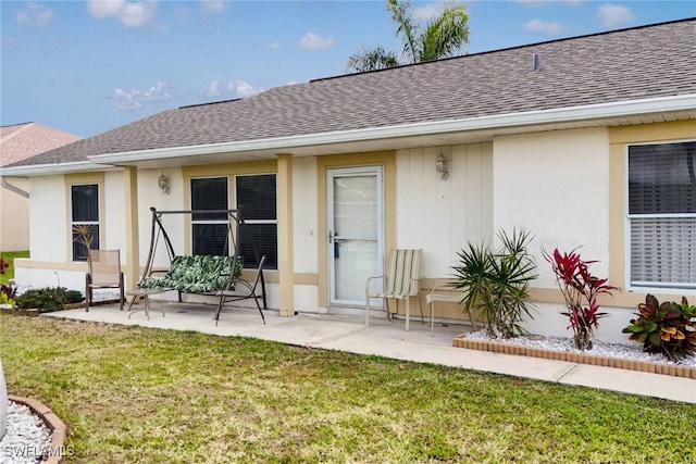 entrance to property with stucco siding, a yard, and a shingled roof