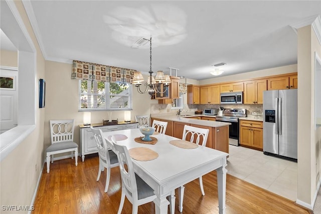 dining room featuring visible vents, light wood finished floors, ornamental molding, a toaster, and a chandelier