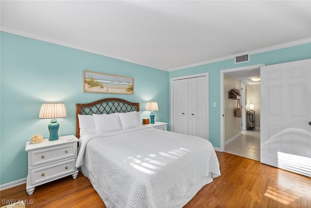 bedroom featuring wood finished floors, visible vents, baseboards, ornamental molding, and a closet