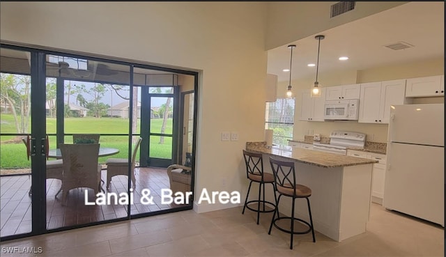 kitchen with visible vents, light stone counters, a kitchen breakfast bar, white cabinetry, and white appliances