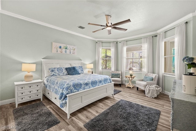 bedroom featuring visible vents, baseboards, wood finished floors, and ornamental molding