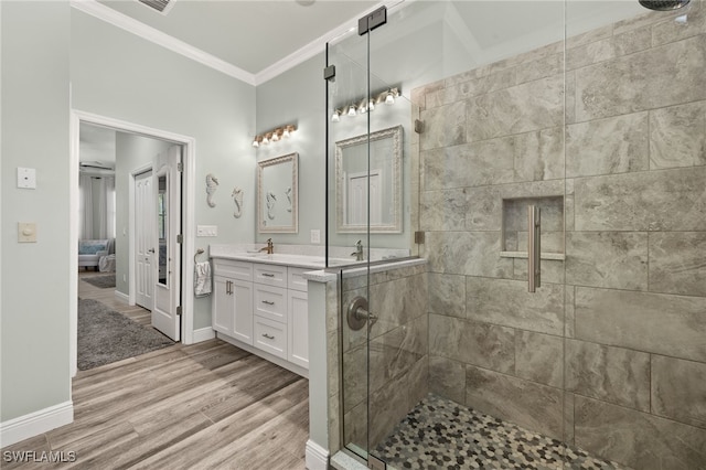 bathroom with wood finished floors, a tile shower, crown molding, double vanity, and baseboards