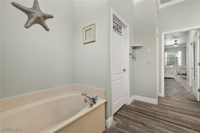 ensuite bathroom featuring a ceiling fan, wood finished floors, baseboards, a garden tub, and connected bathroom