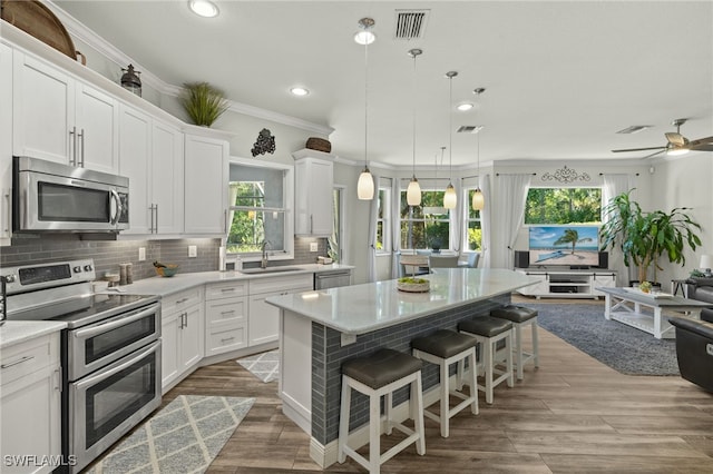 kitchen with visible vents, a sink, a kitchen island, backsplash, and appliances with stainless steel finishes