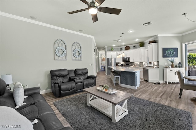 living room with visible vents, crown molding, baseboards, ceiling fan, and wood finished floors