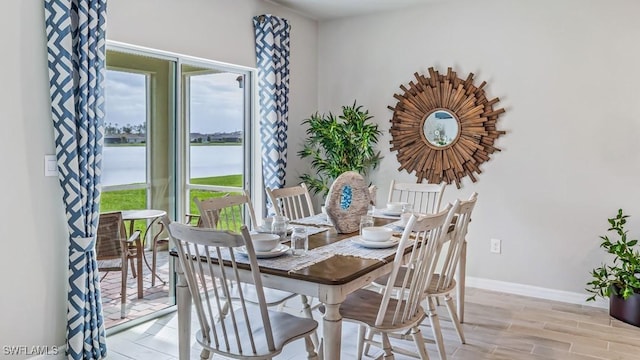 dining space featuring a water view, baseboards, and wood tiled floor