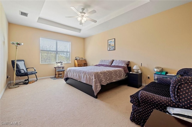 bedroom featuring visible vents, baseboards, a tray ceiling, carpet floors, and a ceiling fan