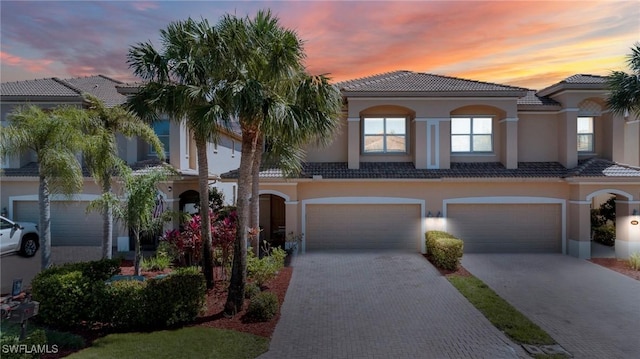 view of front of house with stucco siding, a tiled roof, an attached garage, and decorative driveway