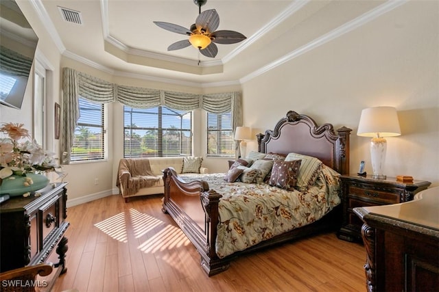 bedroom with multiple windows, crown molding, light wood-style flooring, and a tray ceiling