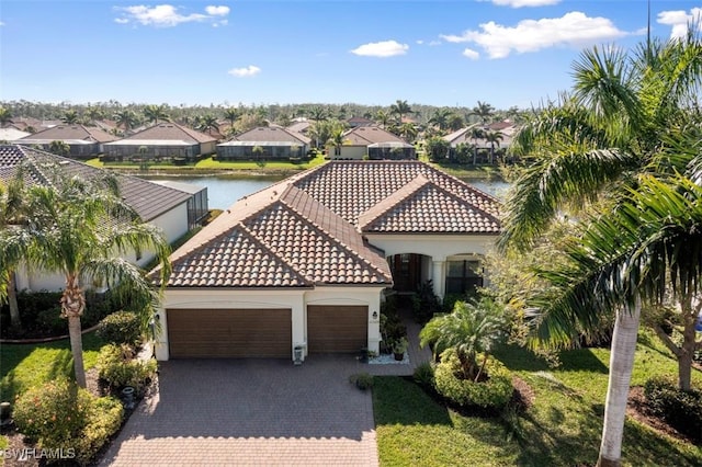 mediterranean / spanish house featuring stucco siding, a garage, a water view, a tiled roof, and decorative driveway