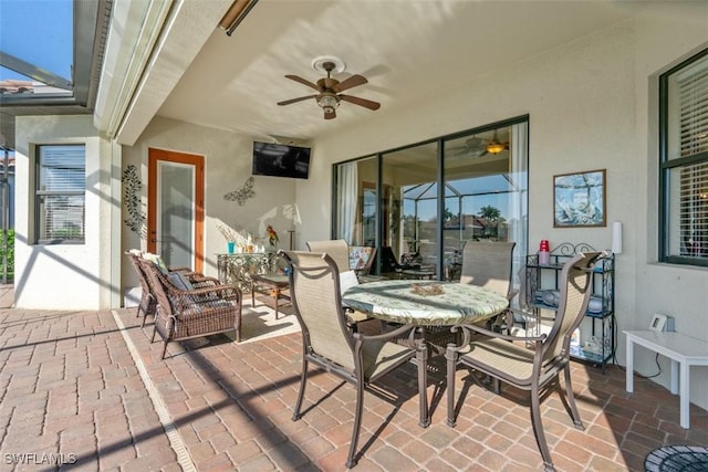 view of patio with glass enclosure, outdoor dining space, and a ceiling fan