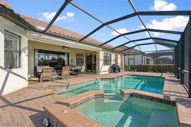 view of swimming pool featuring glass enclosure, a pool with connected hot tub, a ceiling fan, and a patio area