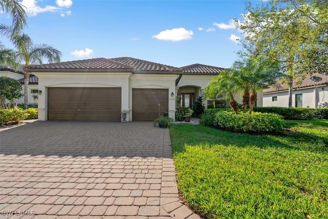 mediterranean / spanish-style house with stucco siding, a tile roof, decorative driveway, a front yard, and an attached garage