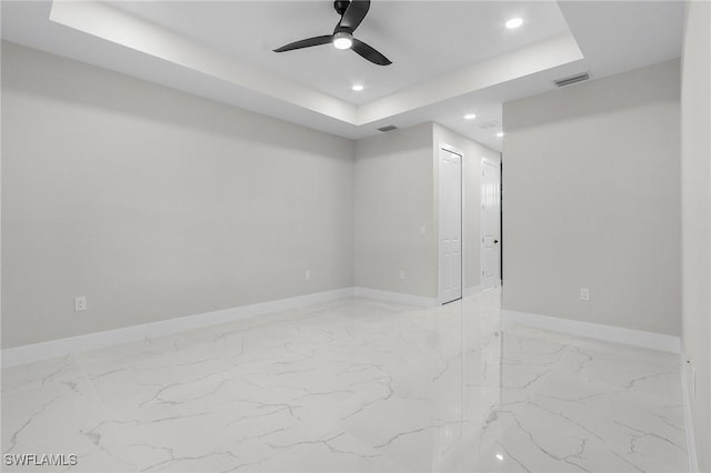 spare room with a tray ceiling, baseboards, visible vents, and ceiling fan