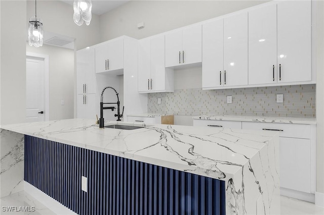 kitchen with light stone countertops, a sink, decorative backsplash, hanging light fixtures, and white cabinetry