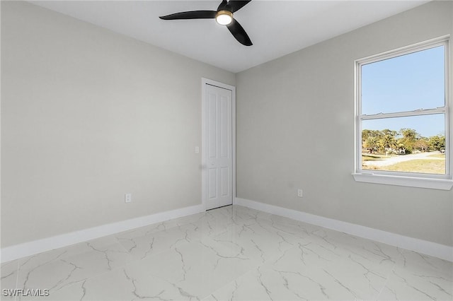 empty room featuring ceiling fan, marble finish floor, and baseboards