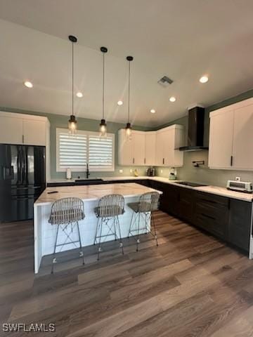 kitchen with a center island, wall chimney range hood, light countertops, white cabinets, and black appliances