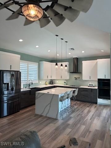 kitchen featuring pendant lighting, a ceiling fan, black fridge, a kitchen island, and wall chimney exhaust hood